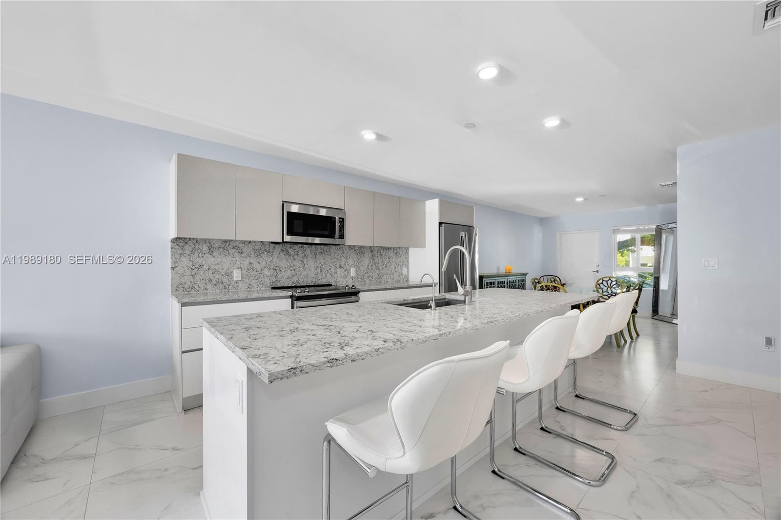 A modern kitchen features a large granite island, white bar stools, and light-colored cabinetry — 2555 NE 193rd St # 2122, Miami FL 33180, MIAMI, FL