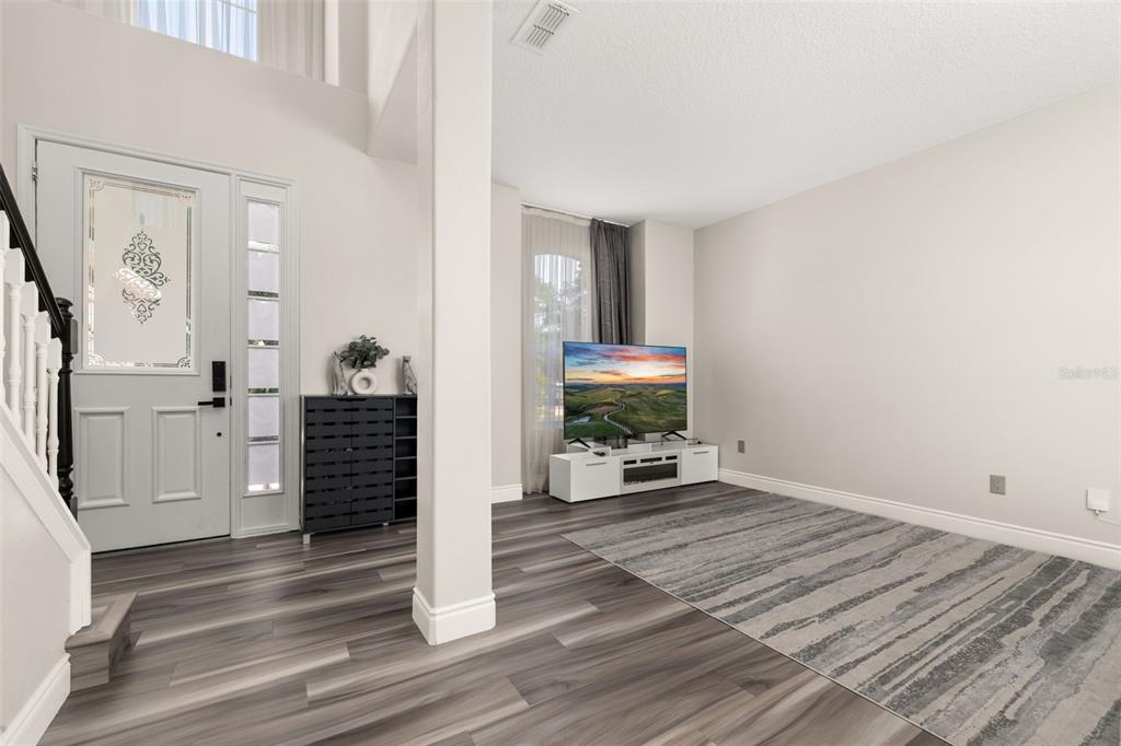 An entryway with wood-look flooring leads into a living area featuring a television and rug — 13247 HATHERTON CIRCLE, ORLANDO, FL