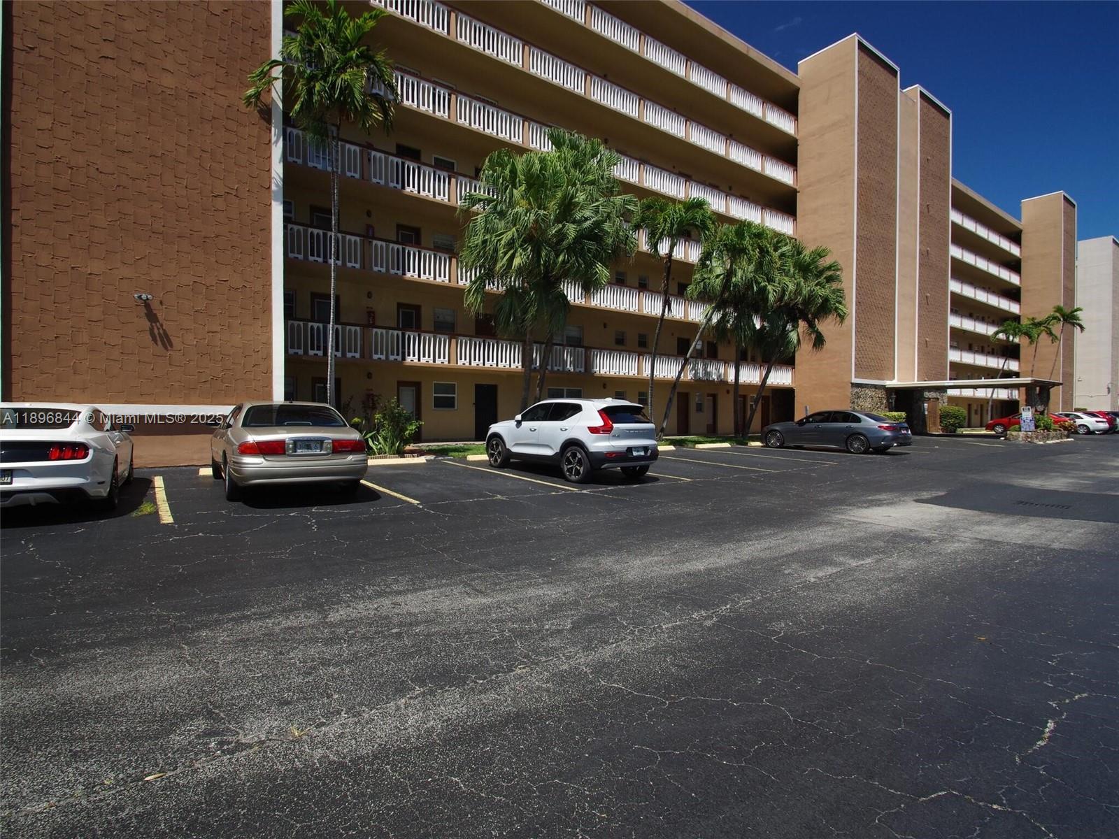 A multi-story apartment building with balconies stands behind a parking lot with several cars — 420 NE 12th Ave # 401, Hallandale Beach FL 33009, HALLANDALE BEACH, FL