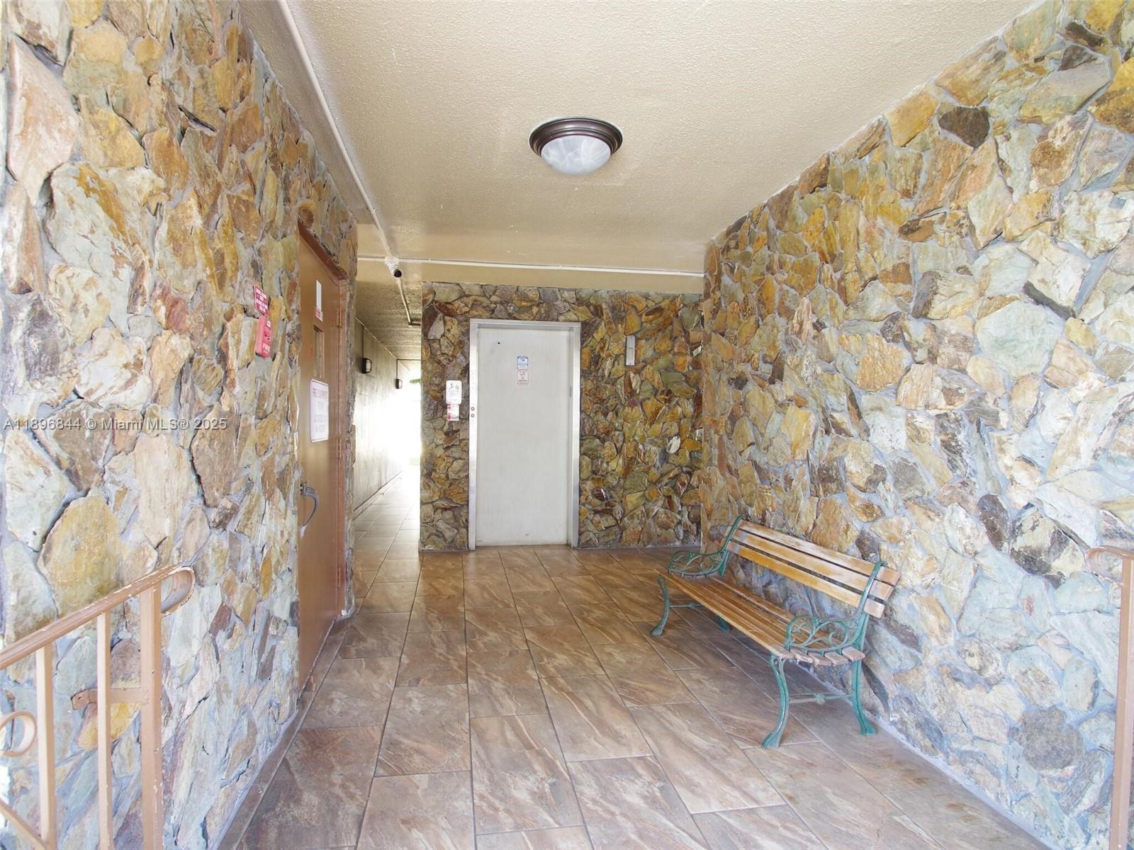A hallway features stone walls, tiled flooring, a wooden bench, and an elevator door — 420 NE 12th Ave # 401, Hallandale Beach FL 33009, HALLANDALE BEACH, FL