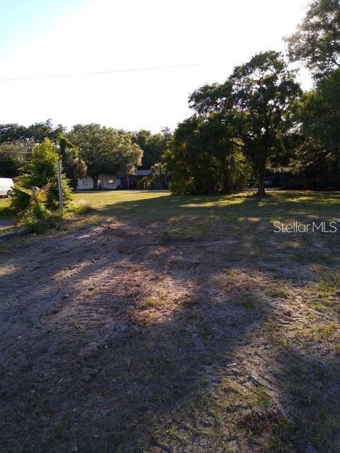 A vacant, grassy lot with tire tracks leads toward trees and a house in the distance — 1512 S MISSOURI AVENUE, CLEARWATER, FL