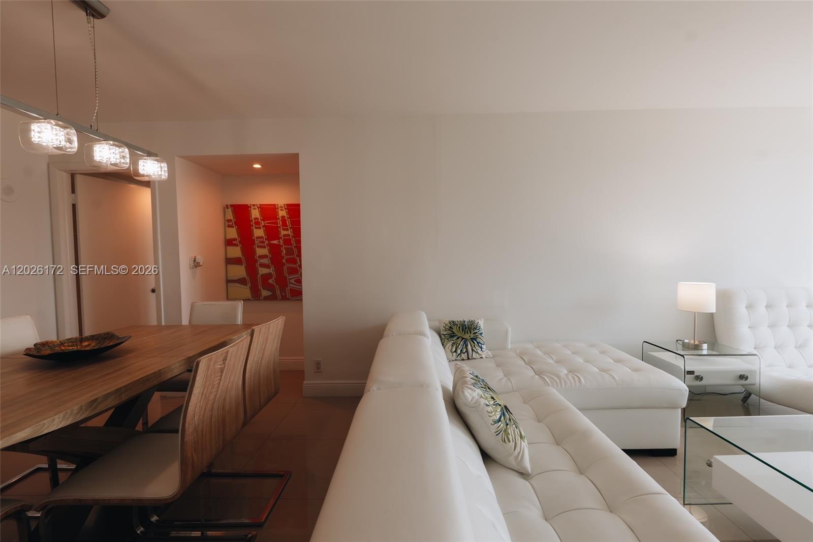 A dining area with a wooden table sits adjacent to a white tufted sectional sofa — 1717 N Bayshore Dr # 1253, Miami FL 33132, MIAMI, FL