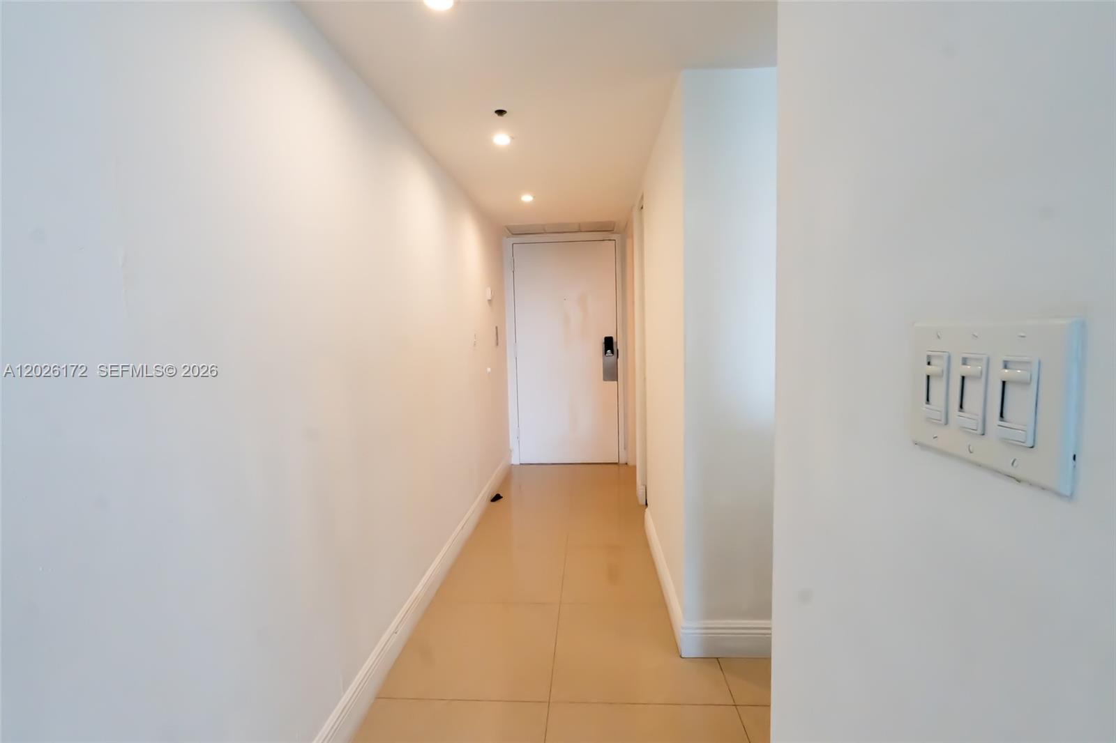 A hallway with white walls, tile flooring, and a light switch panel on the right — 1717 N Bayshore Dr # 1253, Miami FL 33132, MIAMI, FL