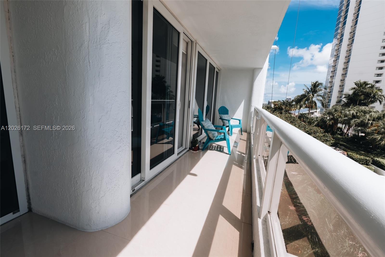 A balcony features light tile flooring, white railings, and two bright blue chairs — 1717 N Bayshore Dr # 1253, Miami FL 33132, MIAMI, FL