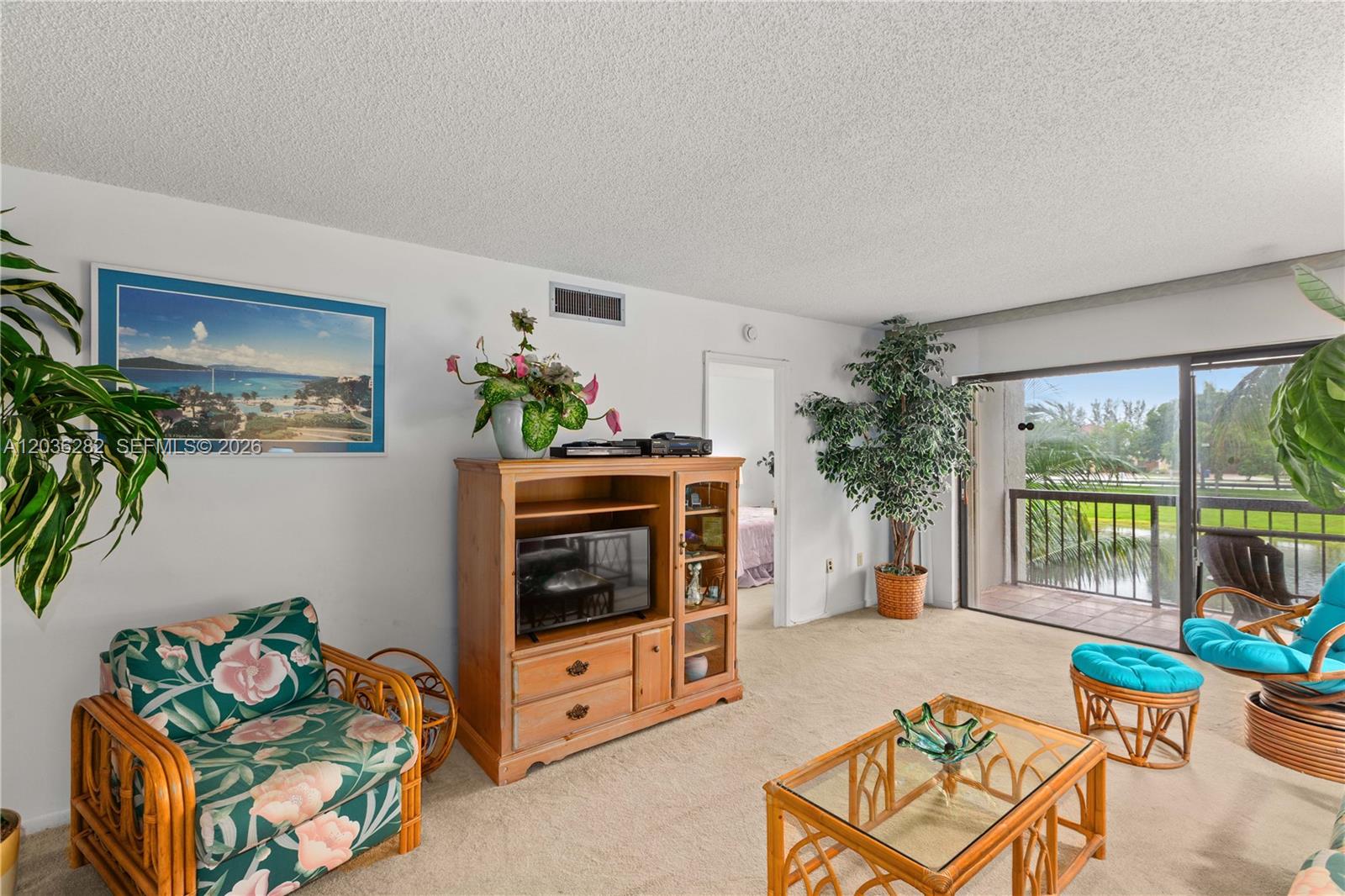 A living room features floral furniture, a wooden entertainment center, and a balcony overlooking water — 10155 NW 9th St Cir # 202, Miami FL 33172, MIAMI, FL