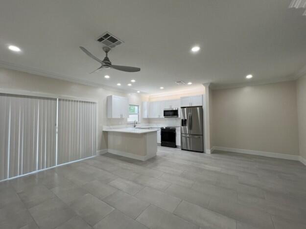 A modern kitchen with white cabinets and stainless steel appliances opens into a tiled living area — 239 Leland Lane, FL 33463, FL