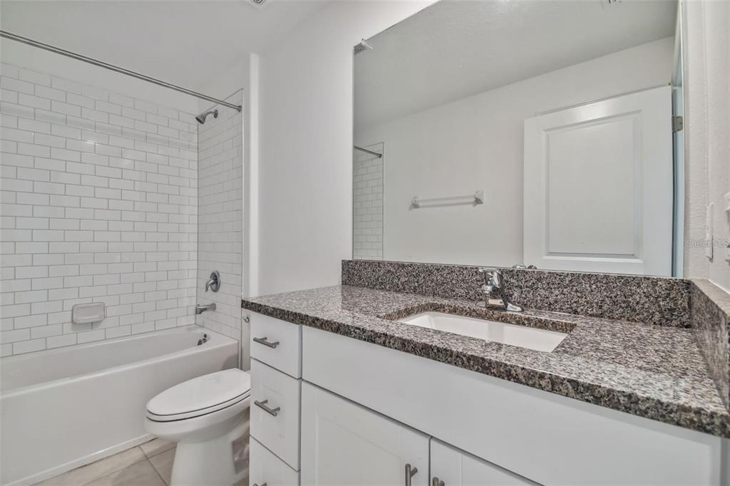 A bathroom features a white vanity with a granite countertop, a toilet, and a tub-shower — 9828 BRANCHING SHIP TRACE TRACE, WESLEY CHAPEL, FL