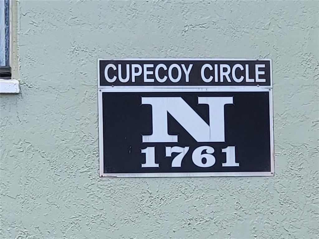 A rectangular sign on a textured wall displays the text Cupecoy Circle N 1761 — 1761 CUPECOY CIRCLE UNIT # N-7, LUTZ, FL