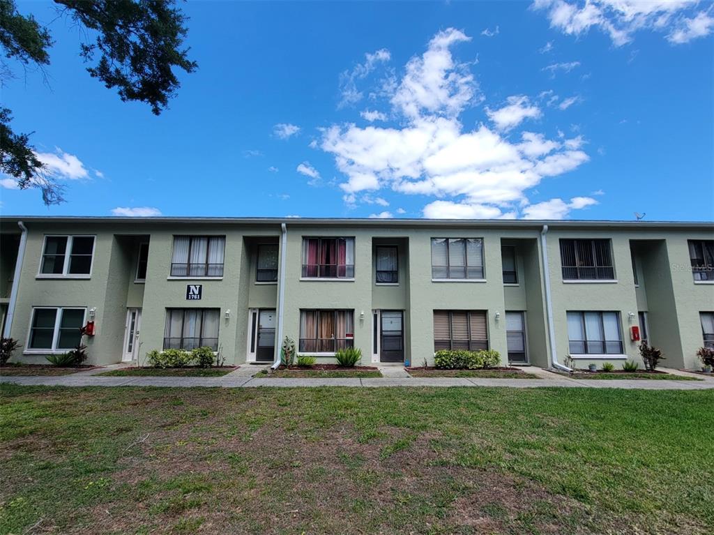 A two-story apartment building exterior features light green stucco walls and a grassy lawn — 1761 CUPECOY CIRCLE UNIT # N-7, LUTZ, FL