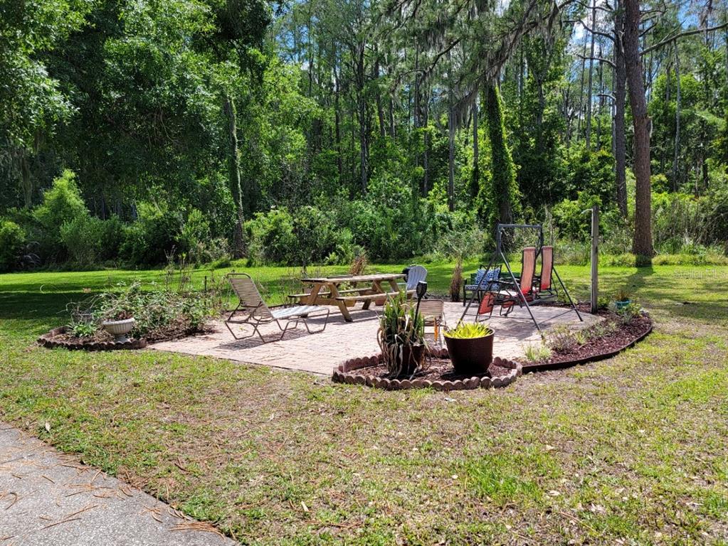 A brick patio with outdoor furniture sits in a grassy backyard surrounded by trees — 1761 CUPECOY CIRCLE UNIT # N-7, LUTZ, FL
