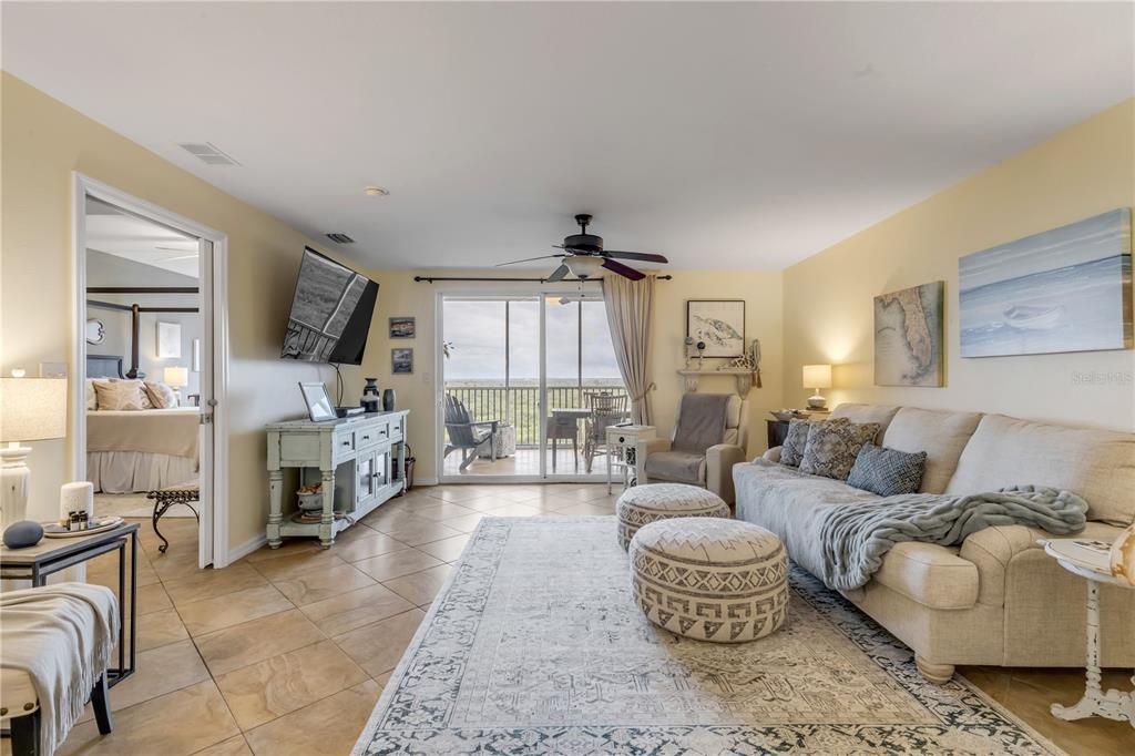 A living room features tile floors, a beige sofa, two ottomans, and a sliding glass door — 5300 S ATLANTIC AVENUE UNIT 16-502, NEW SMYRNA BEACH, FL