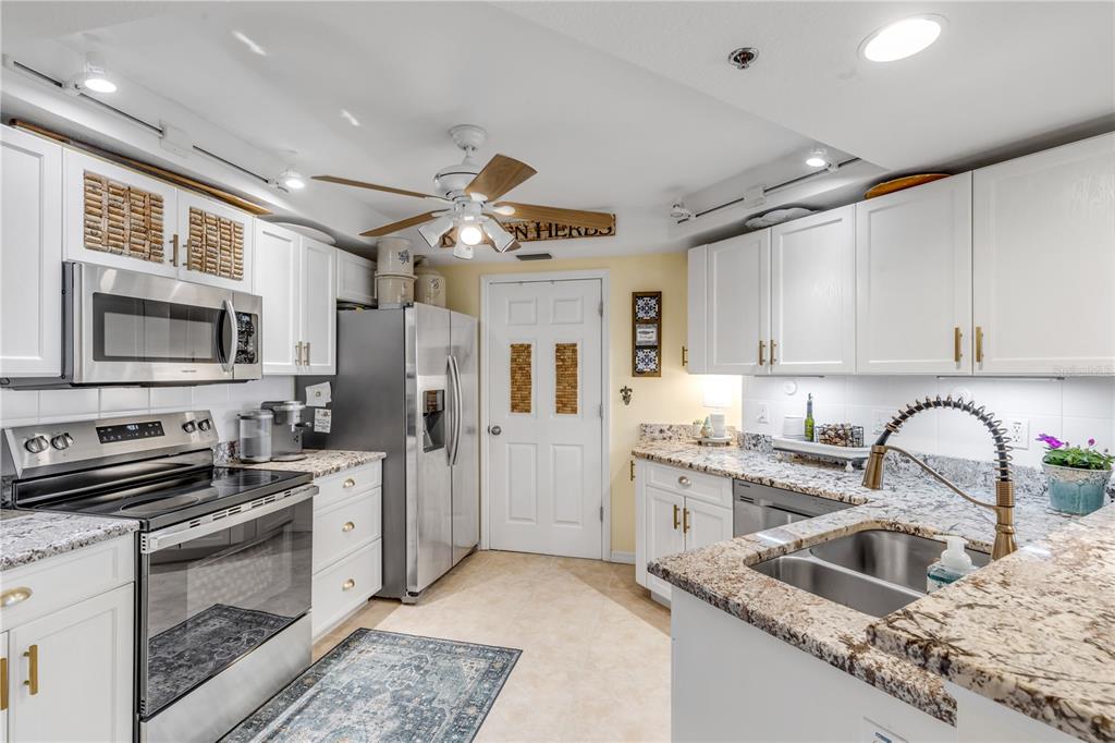 A kitchen features white cabinetry, granite countertops, stainless steel appliances, and a ceiling fan — 5300 S ATLANTIC AVENUE UNIT 16-502, NEW SMYRNA BEACH, FL