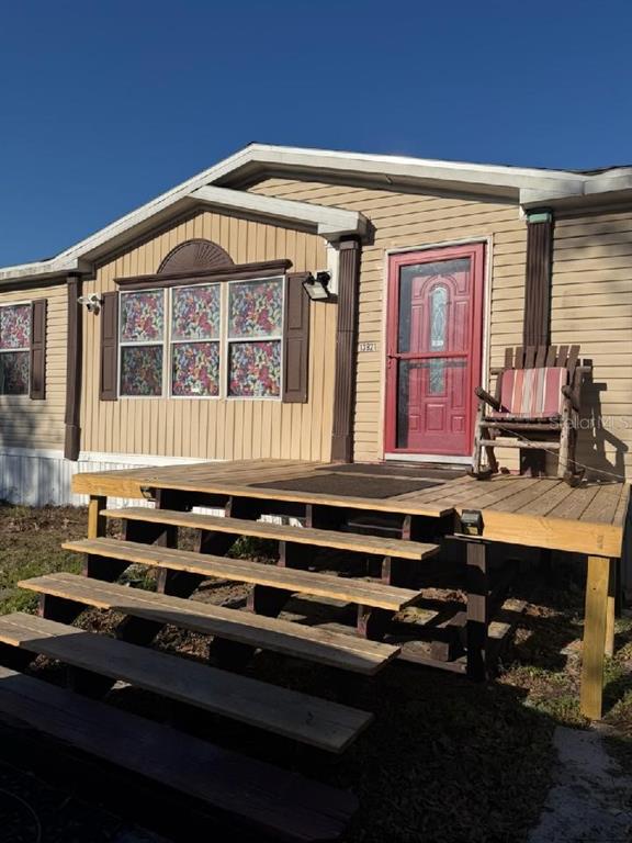 A tan mobile home features a wooden deck with stairs and a red front door — 13921 PINE MEADOW ROAD, KATHLEEN, FL