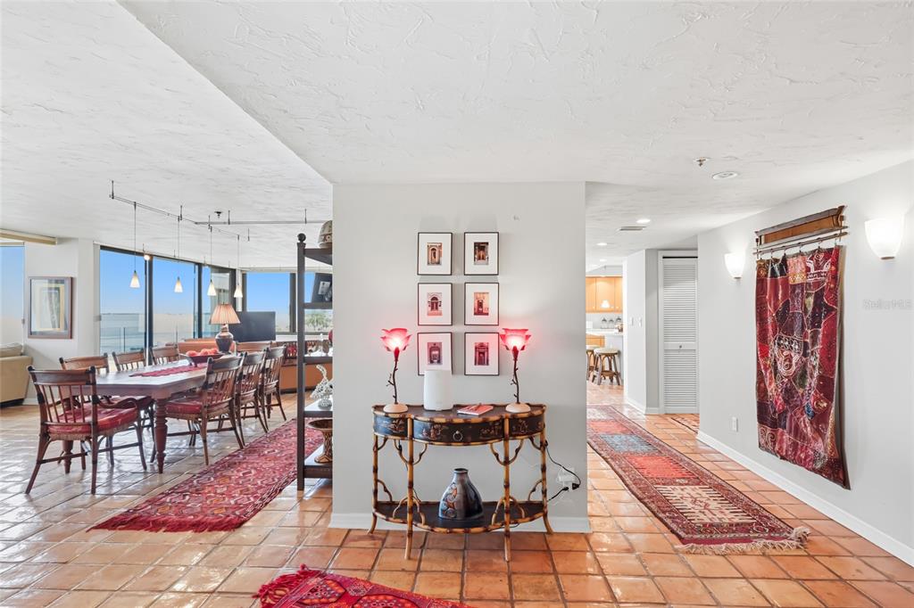 A dining area and hallway feature terracotta tile floors, red patterned rugs, and decorative wall art — 97 SUNSET DRIVE UNIT 501, SARASOTA, FL