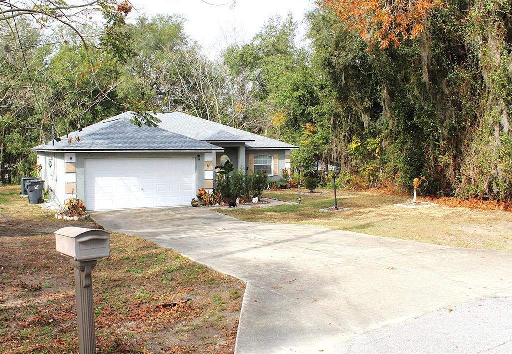 A single-story house with a white garage door and a concrete driveway sits among trees — 42 DOGWOOD DRIVE COURSE, OCALA, FL
