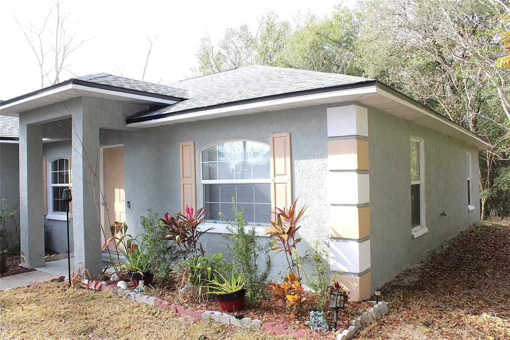 A single-story house with gray stucco siding, a covered entryway, and a small front garden — 42 DOGWOOD DRIVE COURSE, OCALA, FL