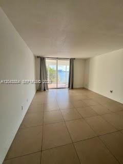 An empty room with beige tile flooring and a sliding glass door overlooking the water — 1100 NE 191st St # 24E, Miami FL 33179, MIAMI, FL