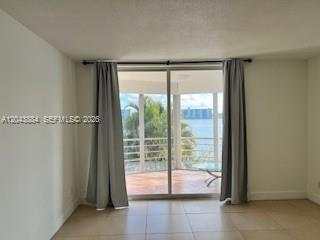 An interior room features light-colored tile floors, gray curtains, and a sliding glass door view — 1100 NE 191st St # 24E, Miami FL 33179, MIAMI, FL