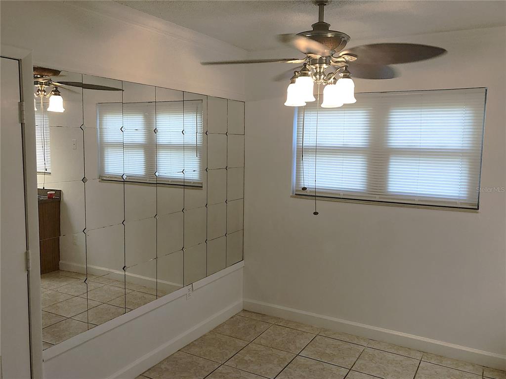 A room with tiled floors, a ceiling fan, and a wall covered in mirrored tiles — 2545 OAK PARK WAY UNIT 118, ORLANDO, FL