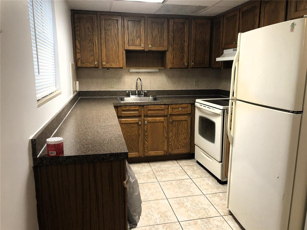 A kitchen features wood cabinets, laminate countertops, white appliances, and light-colored tile flooring — 2545 OAK PARK WAY UNIT 118, ORLANDO, FL
