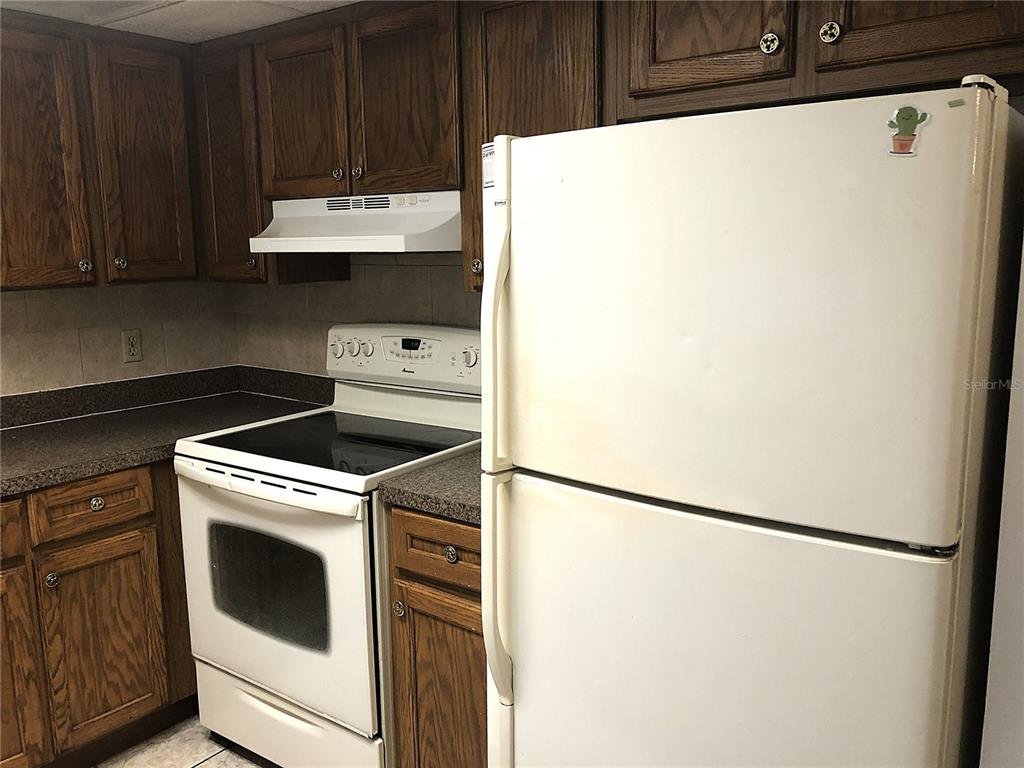 A kitchen features dark wood cabinets, white appliances, and speckled laminate countertops — 2545 OAK PARK WAY UNIT 118, ORLANDO, FL