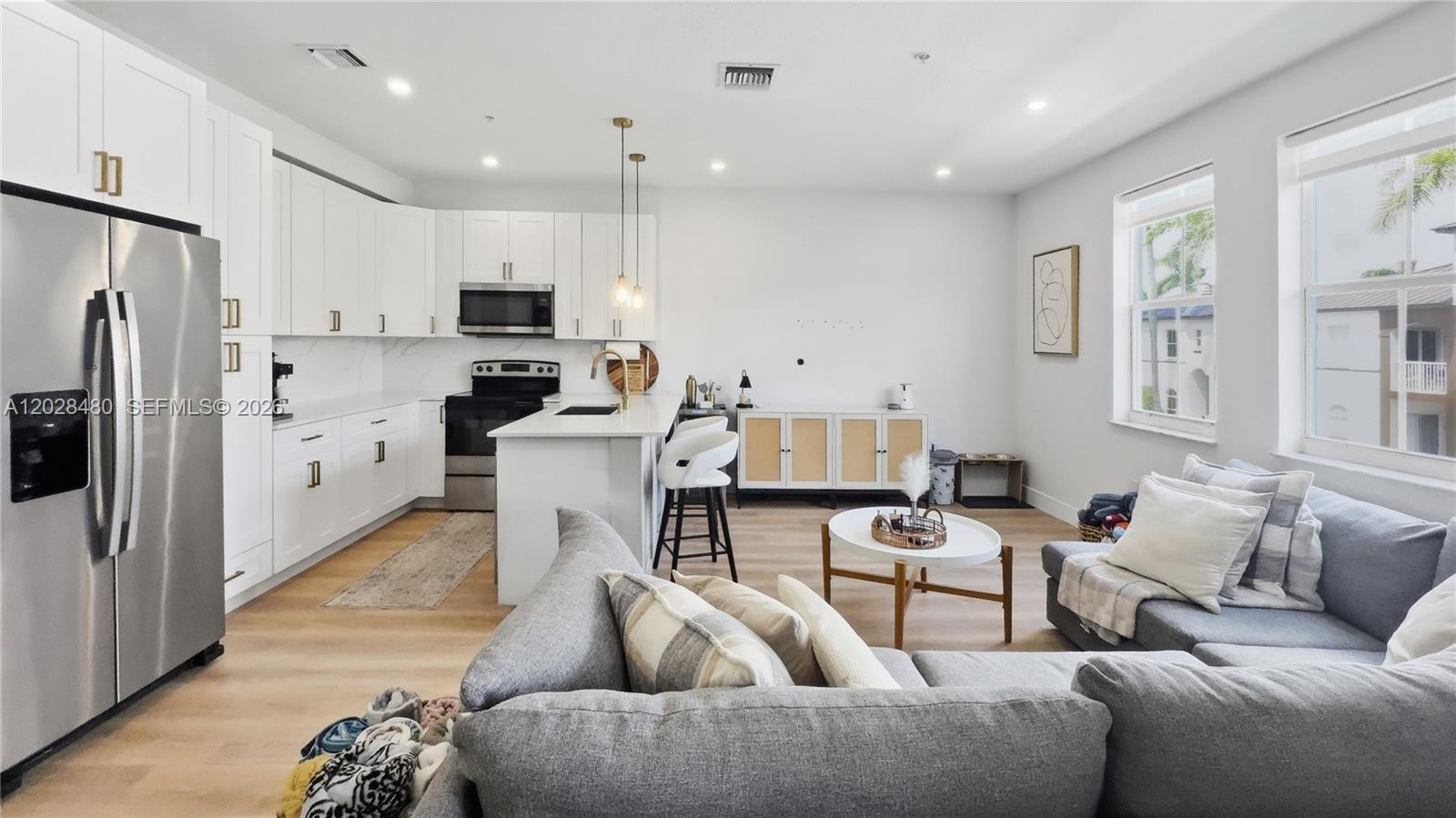 A modern open-concept kitchen and living area features white cabinetry, stainless appliances, and gray furniture — 4425 SW 160th Ave # 213, Miramar FL 33027, MIRAMAR, FL