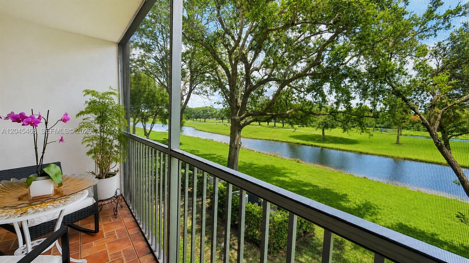 A screened-in balcony overlooks a grassy lawn, a narrow canal, and several mature trees — 1151 SW 128th Ter # 206D, Pembroke Pines FL 33027, PEMBROKE PINES, FL