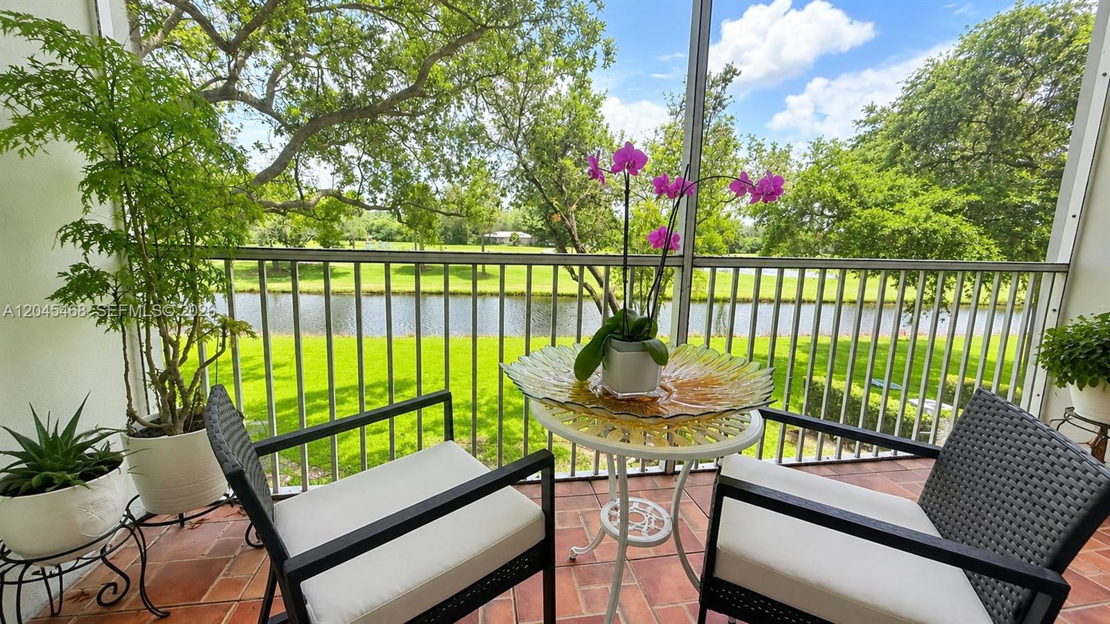 A screened-in balcony features two chairs, a small table with orchids, and a water view — 1151 SW 128th Ter # 206D, Pembroke Pines FL 33027, PEMBROKE PINES, FL