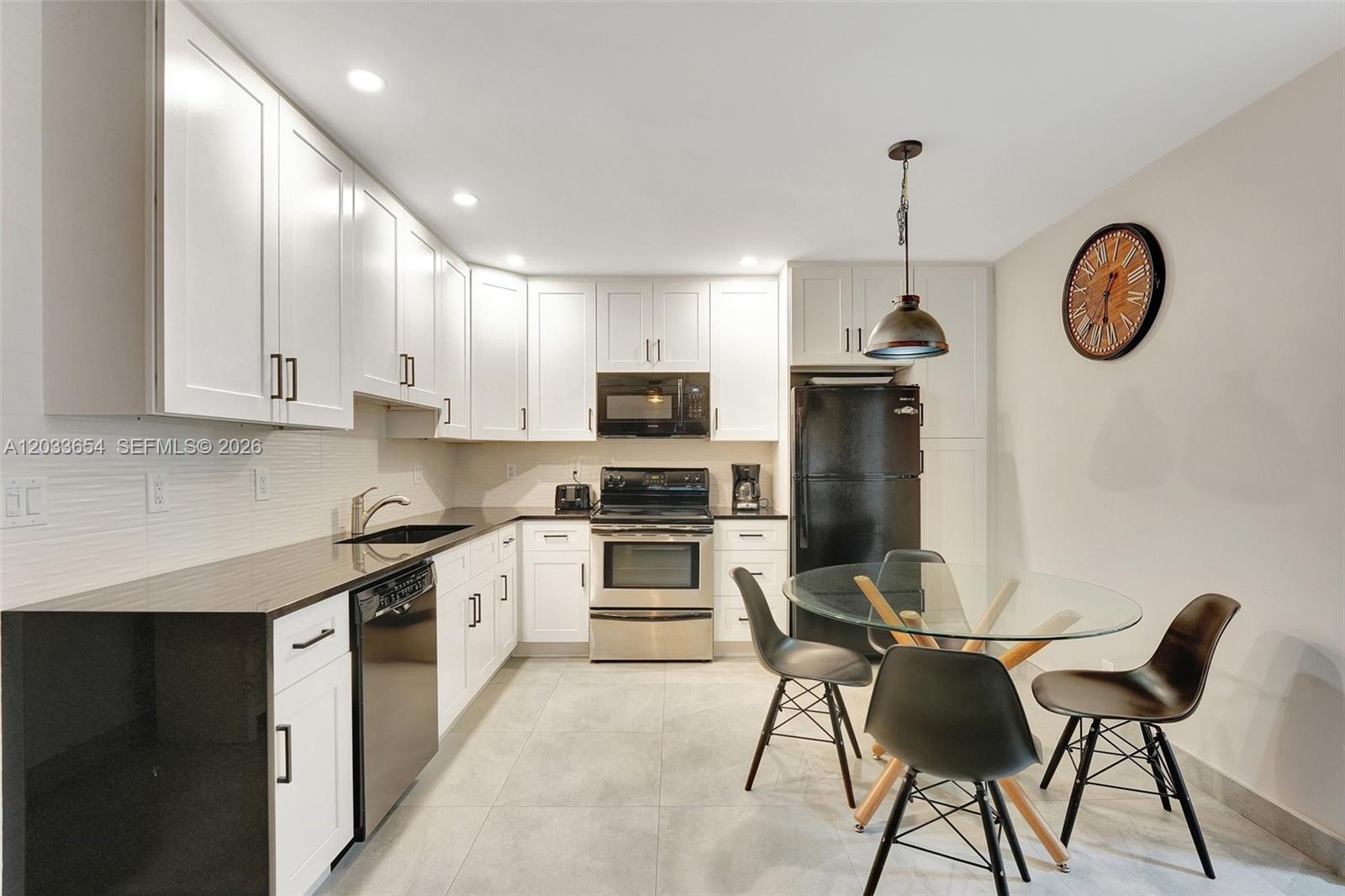A kitchen features white cabinetry, black countertops, stainless steel appliances, and a glass dining table — 221 SE 9th Ave # 102, Pompano Beach FL 33060, POMPANO BEACH, FL