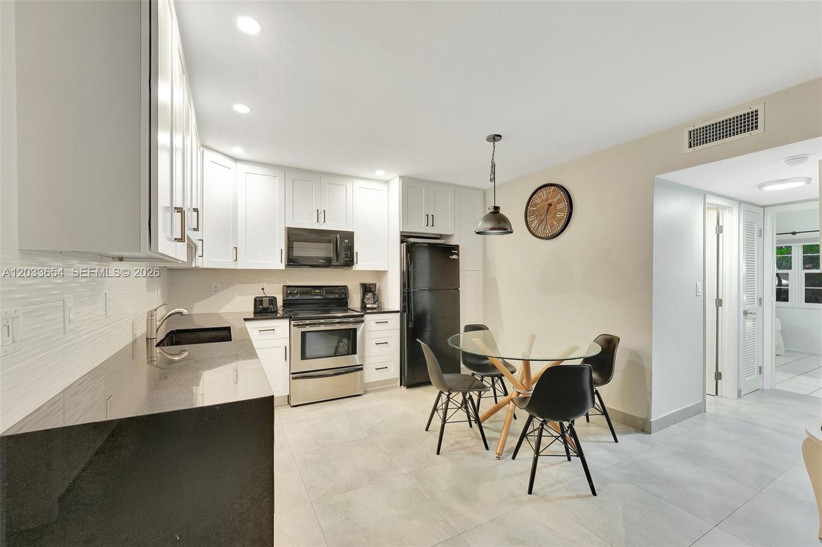 A kitchen features white cabinets, black countertops, stainless steel appliances, and a glass dining table — 221 SE 9th Ave # 102, Pompano Beach FL 33060, POMPANO BEACH, FL