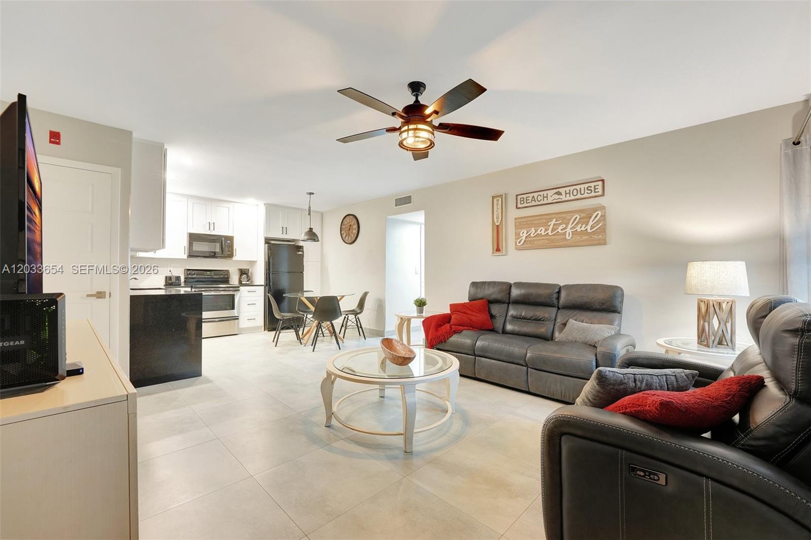 An open-concept living room and kitchen featuring gray leather furniture and light tile flooring — 221 SE 9th Ave # 102, Pompano Beach FL 33060, POMPANO BEACH, FL