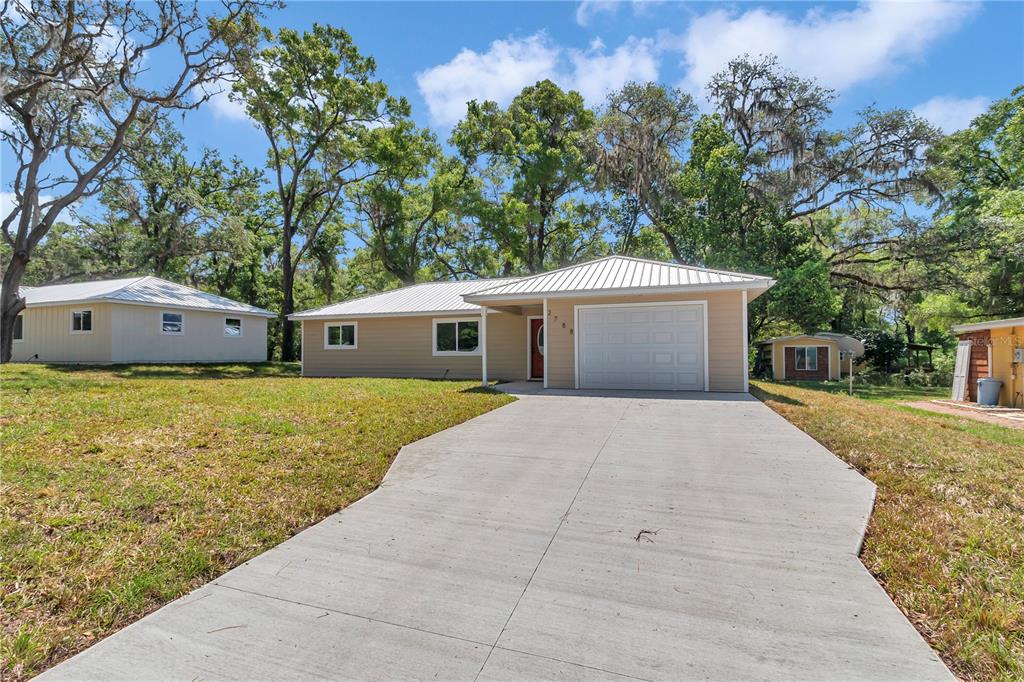 A single-story house with tan siding, a metal roof, and a concrete driveway — 2788 W CYPRESS DRIVE, DUNNELLON, FL