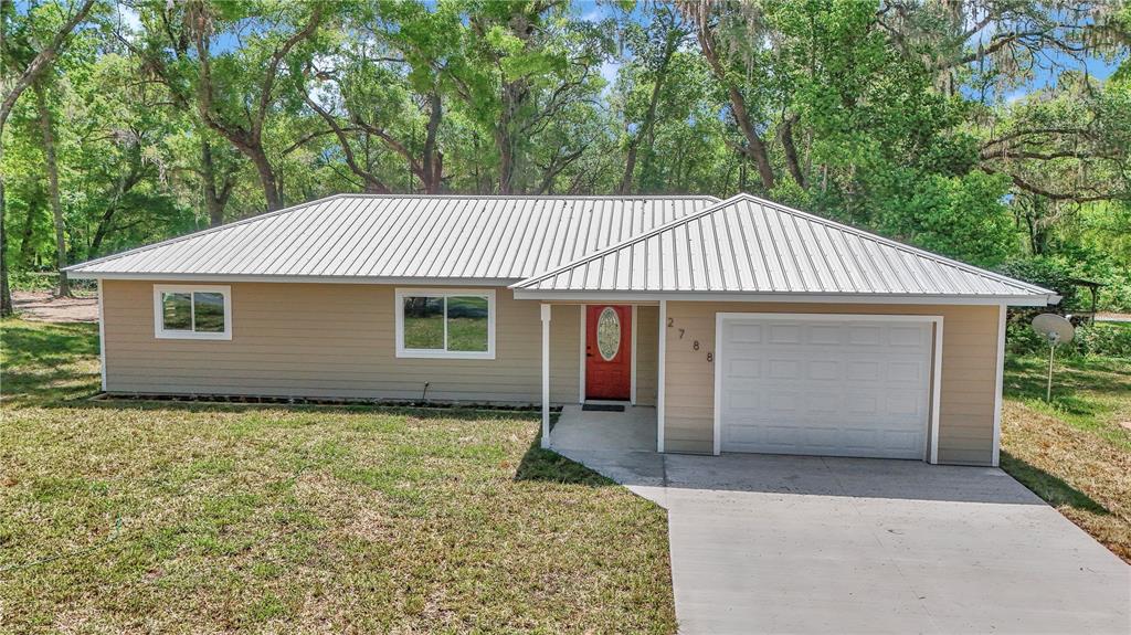 A single-story house with tan siding, a metal roof, a red front door, and a garage — 2788 W CYPRESS DRIVE, DUNNELLON, FL