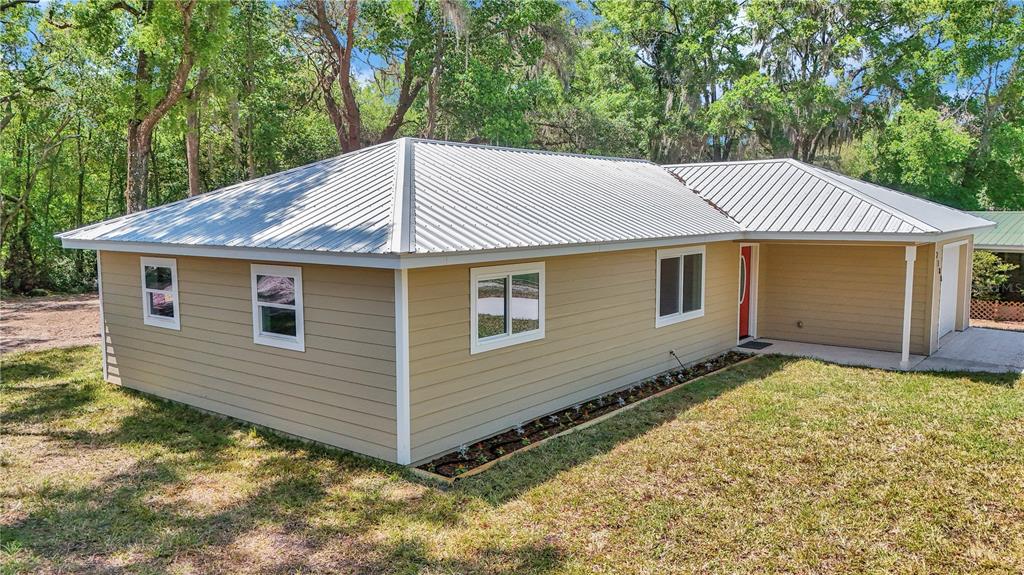 A tan, single-story house with a metal roof sits on a grassy lot with trees — 2788 W CYPRESS DRIVE, DUNNELLON, FL