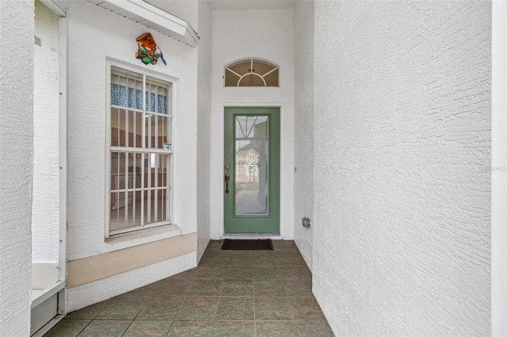 A covered entryway features a green front door, a large window, and tiled flooring — 18452 FAIRWAY GREEN DRIVE, HUDSON, FL
