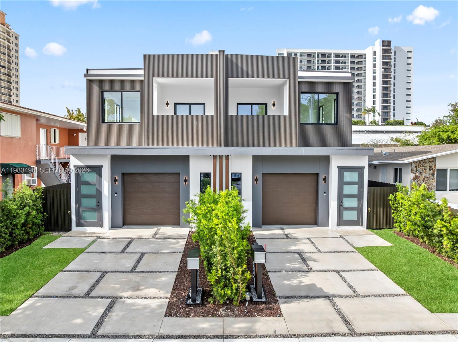 A modern two-story duplex features dark wood-slat siding, two garages, and a shared concrete driveway — 3187 SW 23rd St, Miami FL 33145, MIAMI, FL
