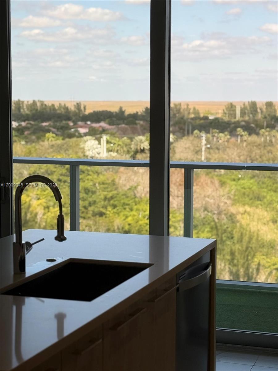 A kitchen island with a dark sink and faucet overlooks a balcony and landscape — 2000 Metropica Way # 901, Sunrise FL 33323, SUNRISE, FL