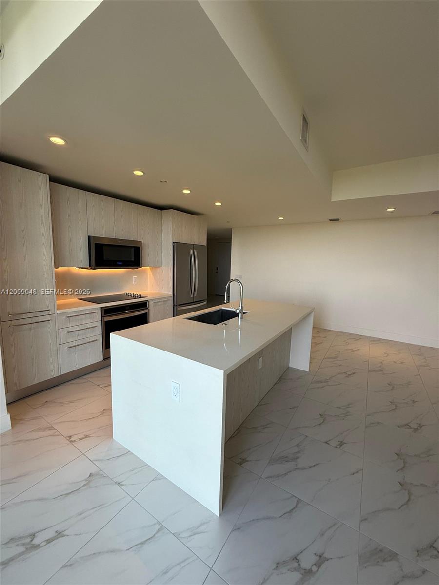 A modern kitchen features light wood cabinetry, a white quartz island, and marble-patterned tile flooring — 2000 Metropica Way # 901, Sunrise FL 33323, SUNRISE, FL
