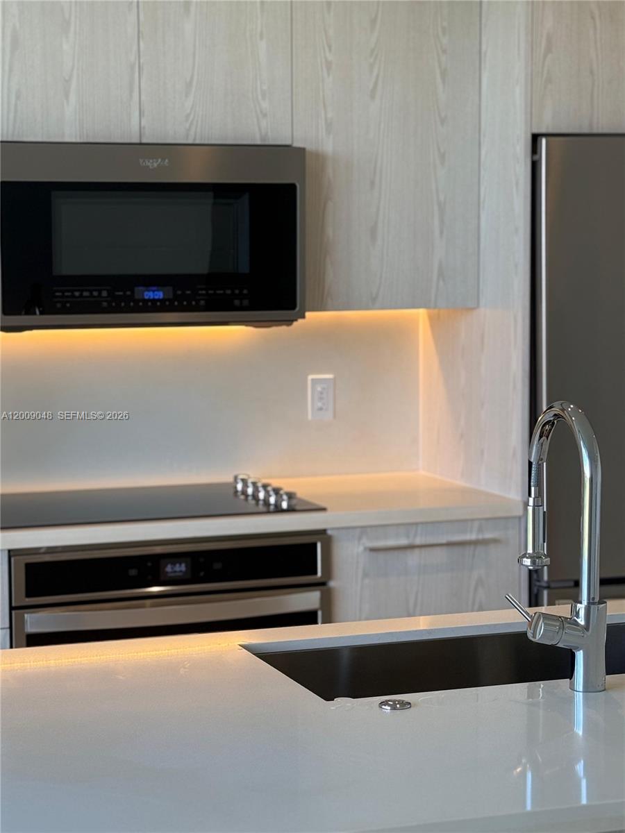 A modern kitchen features light wood cabinetry, stainless steel appliances, and a white quartz countertop — 2000 Metropica Way # 901, Sunrise FL 33323, SUNRISE, FL