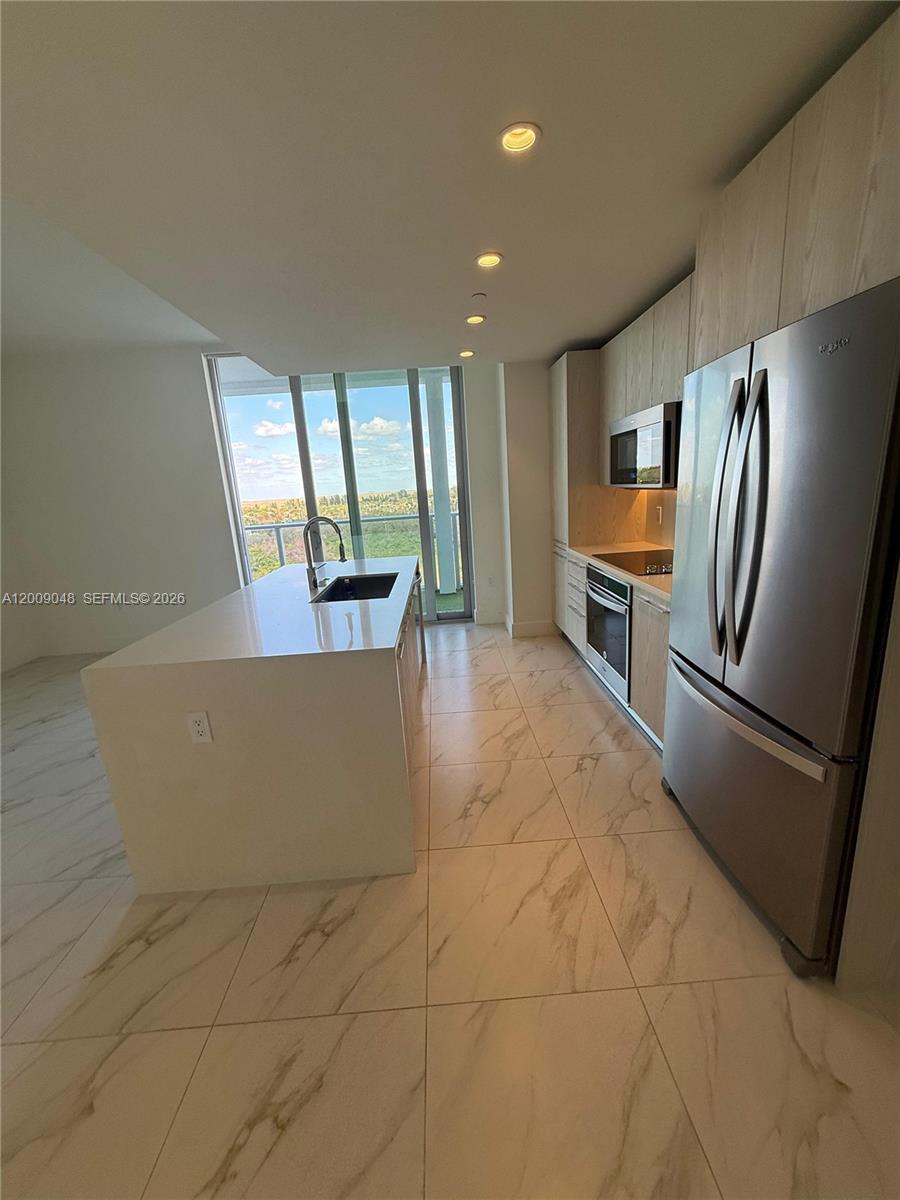 A modern kitchen features a white island, stainless steel appliances, and light-colored marble-patterned tile floors — 2000 Metropica Way # 901, Sunrise FL 33323, SUNRISE, FL
