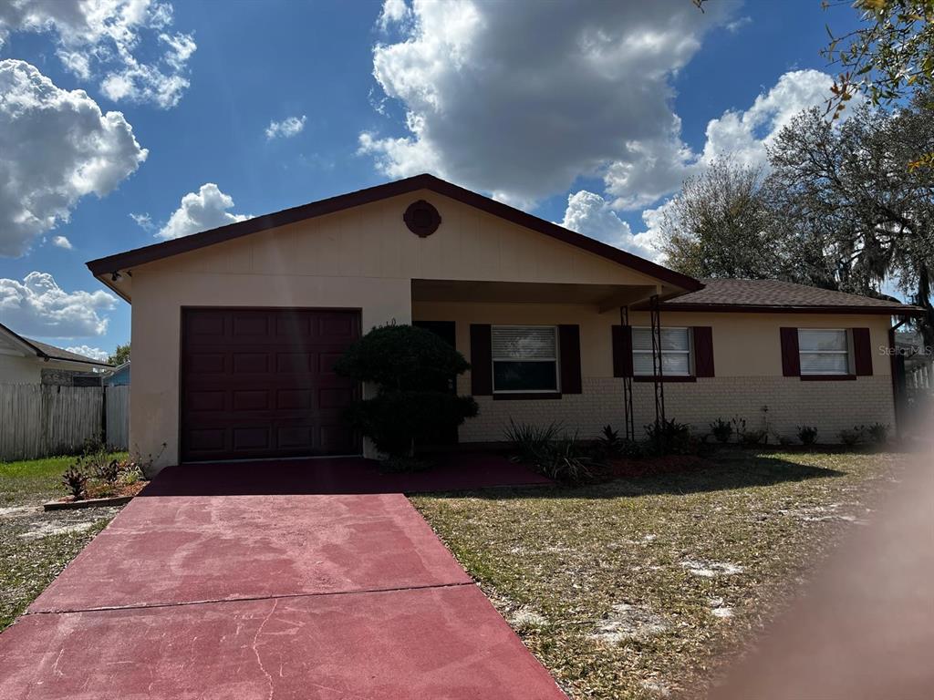 A single-story house with a red driveway, a garage, and brown shutters under a cloudy sky — 4810 LEPRECHAUN WAY, ORLANDO, FL