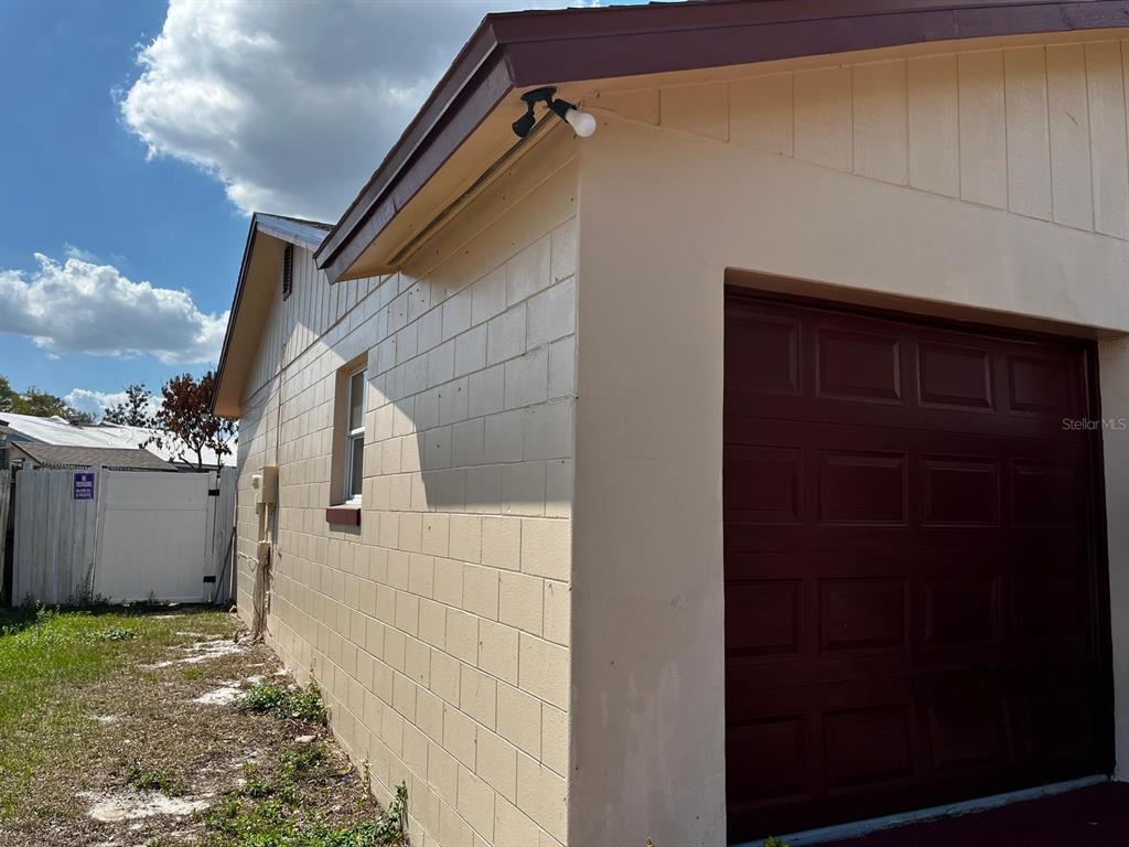A side view of a beige concrete block house with a dark red garage door — 4810 LEPRECHAUN WAY, ORLANDO, FL