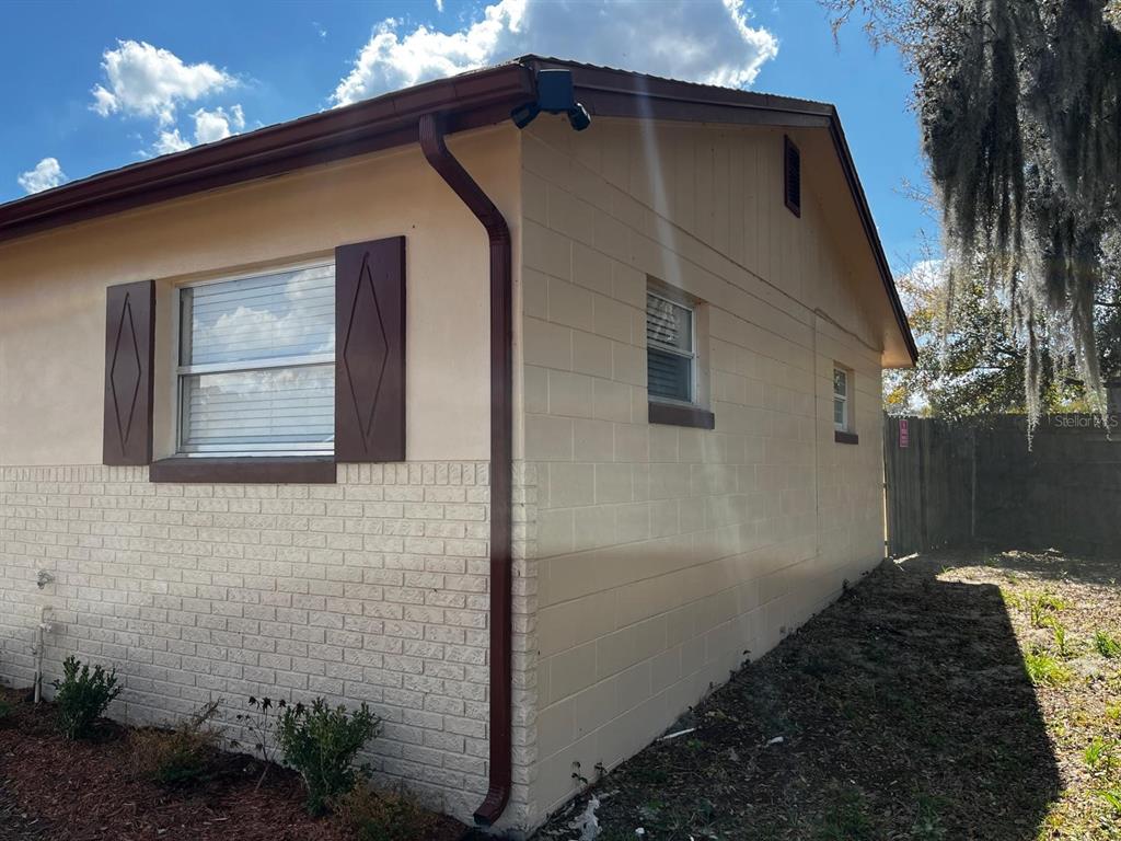 A side view of a house with beige stucco walls, brick accents, and brown trim — 4810 LEPRECHAUN WAY, ORLANDO, FL
