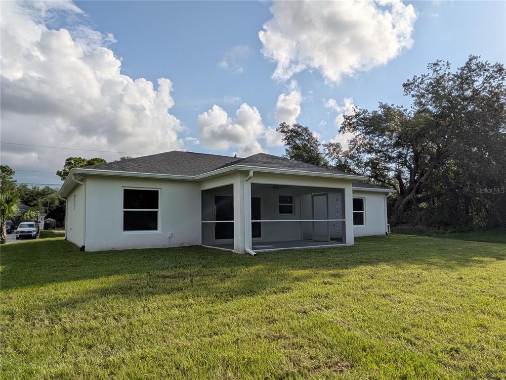 The exterior of a white stucco house features a screened-in back porch and a grassy yard — 6221 LACHINE AVENUE, NORTH PORT, FL