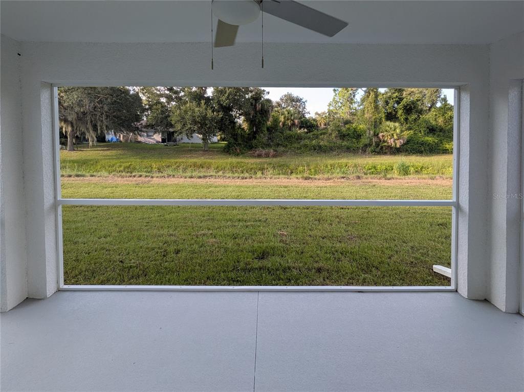 A screened-in patio overlooks a grassy backyard with trees and a distant house — 6221 LACHINE AVENUE, NORTH PORT, FL