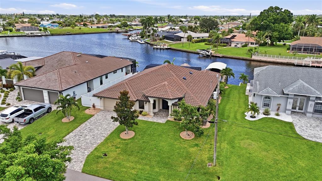 An aerial view shows three houses with tiled roofs situated along a canal with boats — 3221 SE 10TH AVENUE, CAPE CORAL, FL