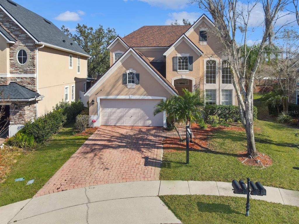 A two-story suburban house with a brick driveway, a two-car garage, and tan stucco siding — 408 RIVER SONG COURT, ORLANDO, FL