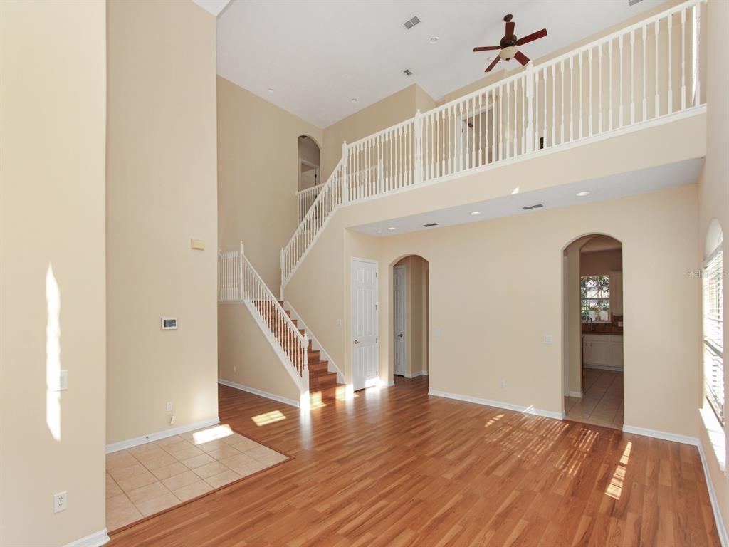 A two-story living room with hardwood floors, a staircase, and a balcony overlooking the space — 408 RIVER SONG COURT, ORLANDO, FL
