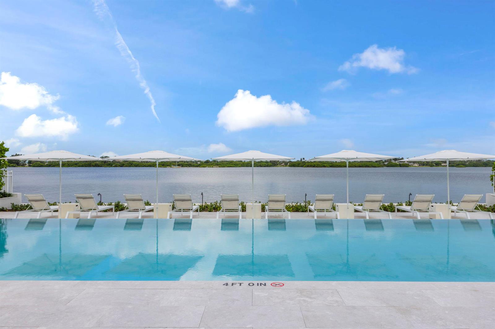 An infinity pool overlooks a calm body of water with lounge chairs and umbrellas — 2773 S Ocean Boulevard # 214, Palm Beach FL 33480, PALM BEACH, FL