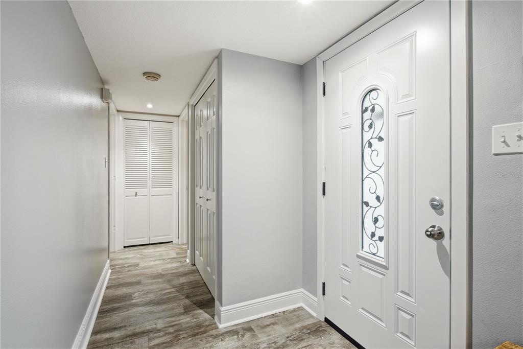 An entryway features light gray walls, wood-look flooring, a white front door, and closet doors — 1144 WOODBROOK DRIVE, LARGO, FL